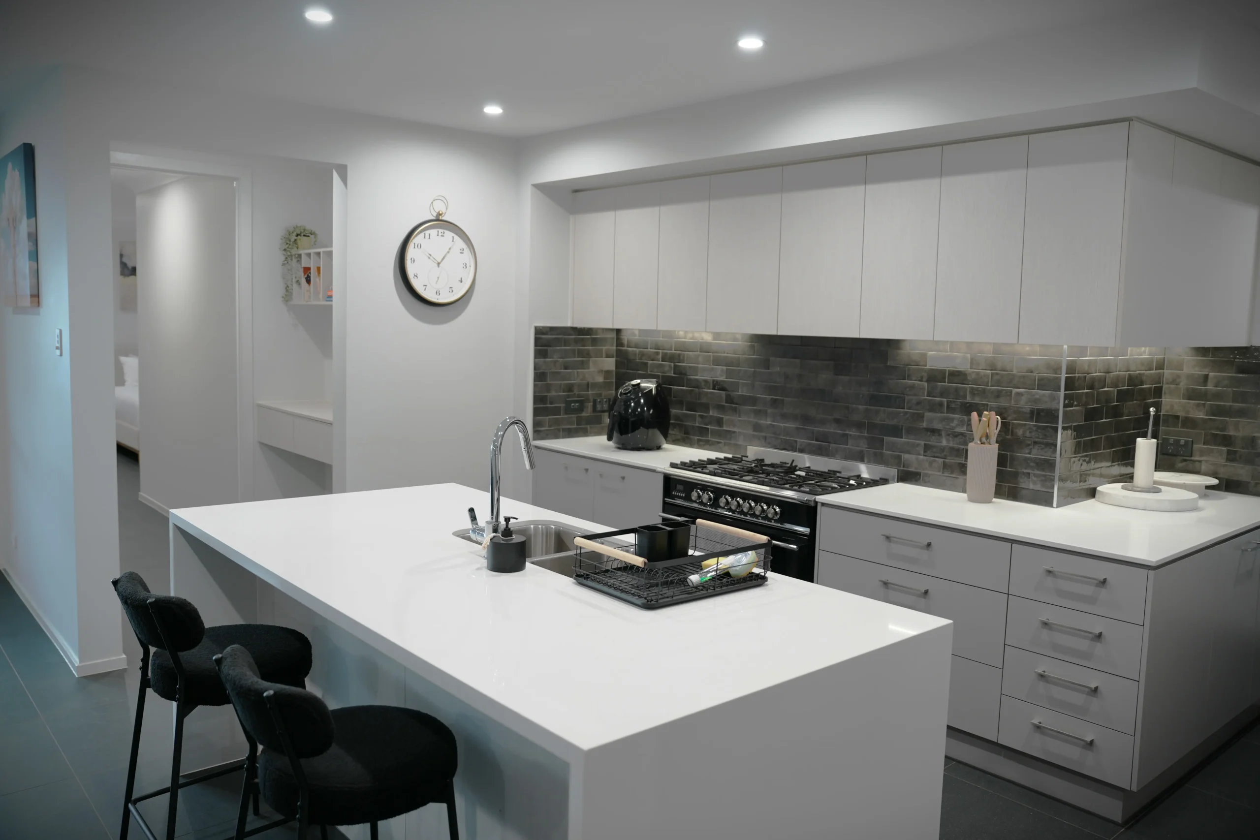 Greenbank Oasis kitchen with white stone island bench, gas cooktop and view through to the bedroom — fully equipped for extended stays