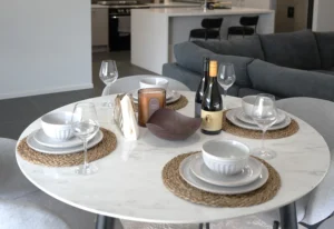 Dining table set for four at Greenbank Oasis SafeStayz accommodation in Brisbane southside, with marble tabletop, full dinnerware and view through to kitchen and lounge