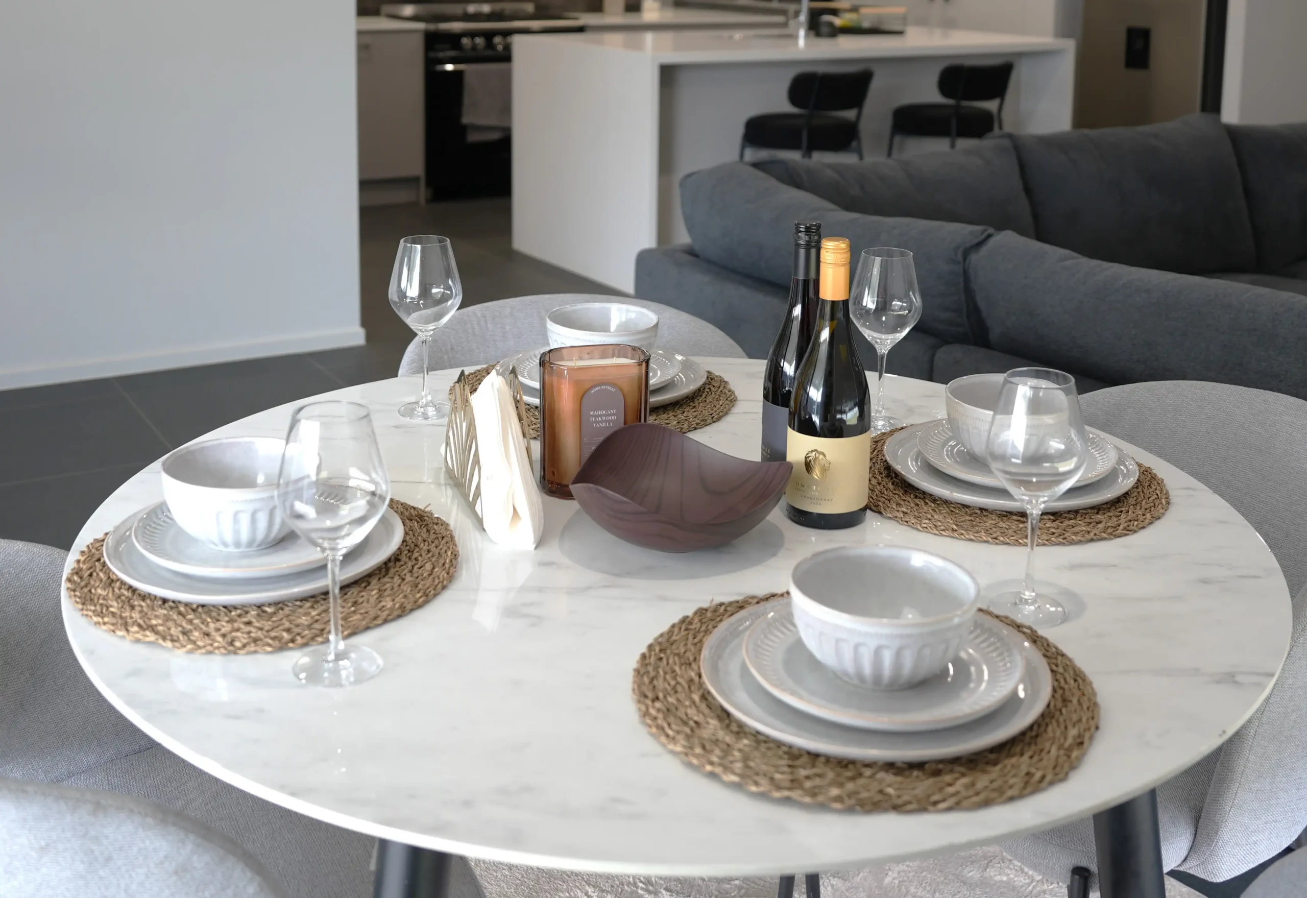 Dining table set for four at Greenbank Oasis SafeStayz accommodation in Brisbane southside, with marble tabletop, full dinnerware and view through to kitchen and lounge
