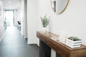 Welcoming entryway at Greenbank Oasis SafeStayz accommodation in Brisbane southside, with timber console table, round mirror and hallway leading through to open-plan living areas