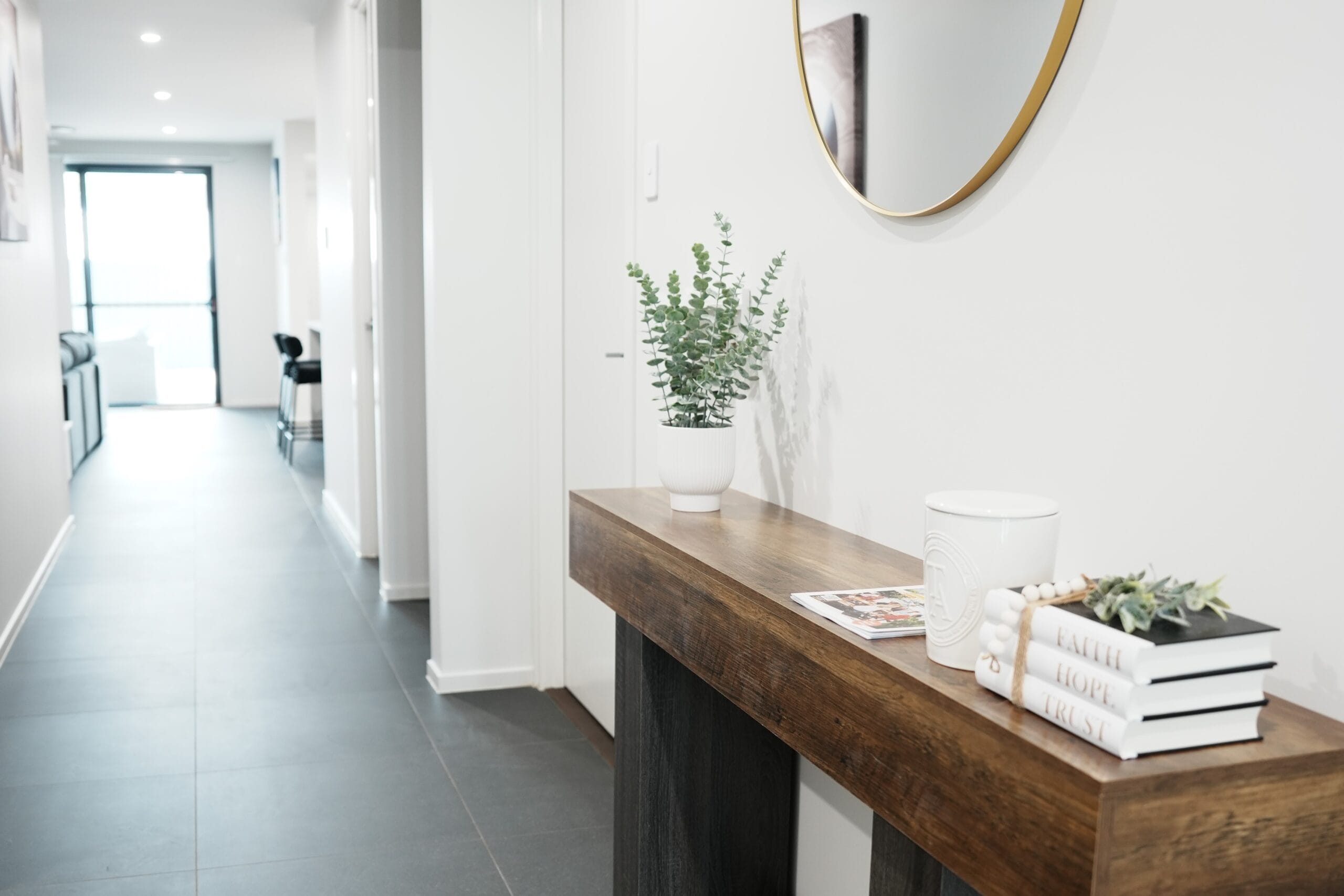 Welcoming entryway at Greenbank Oasis SafeStayz accommodation in Brisbane southside, with timber console table, round mirror and hallway leading through to open-plan living areas