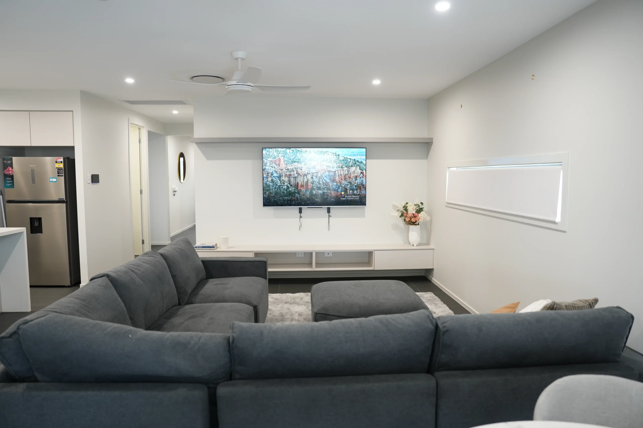 Open-plan living room at Greenbank Oasis SafeStayz accommodation in Brisbane southside, with large modular sofa, wall-mounted smart TV and ceiling fan