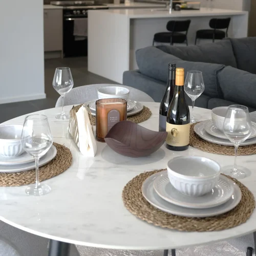 Dining table set for four at Greenbank Oasis SafeStayz accommodation in Brisbane southside, with marble tabletop, full dinnerware and view through to kitchen and lounge