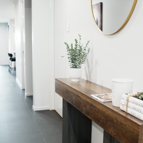 Welcoming entryway at Greenbank Oasis SafeStayz accommodation in Brisbane southside, with timber console table, round mirror and hallway leading through to open-plan living areas