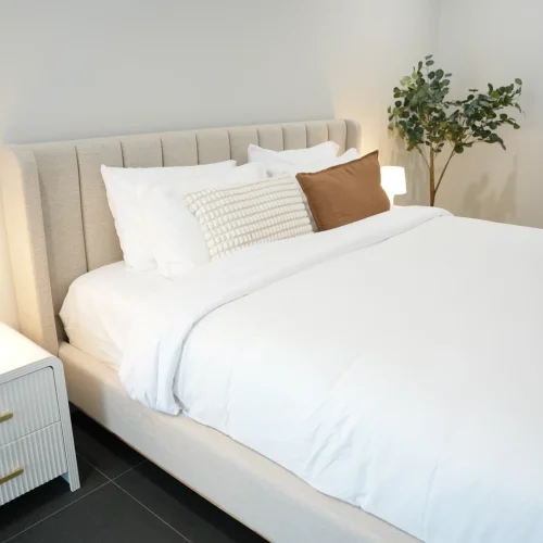 Styled queen bed in second bedroom at Greenbank Oasis SafeStayz accommodation in Brisbane southside, with upholstered headboard, fluted bedside table and crisp white linen